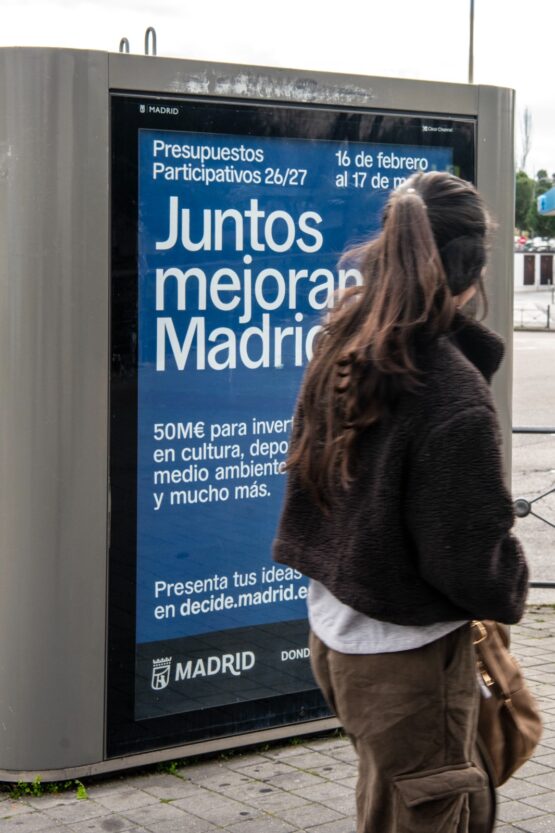 Una joven lee un mupi de presupuestos participativos en una calle de Madrid