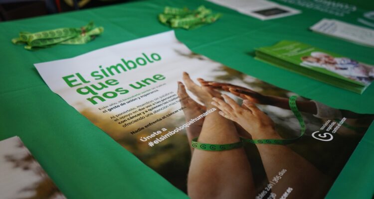 Merchandising y folletos informativos de la iniciativa de la AECC en color verde sobre una mesa de la asociación