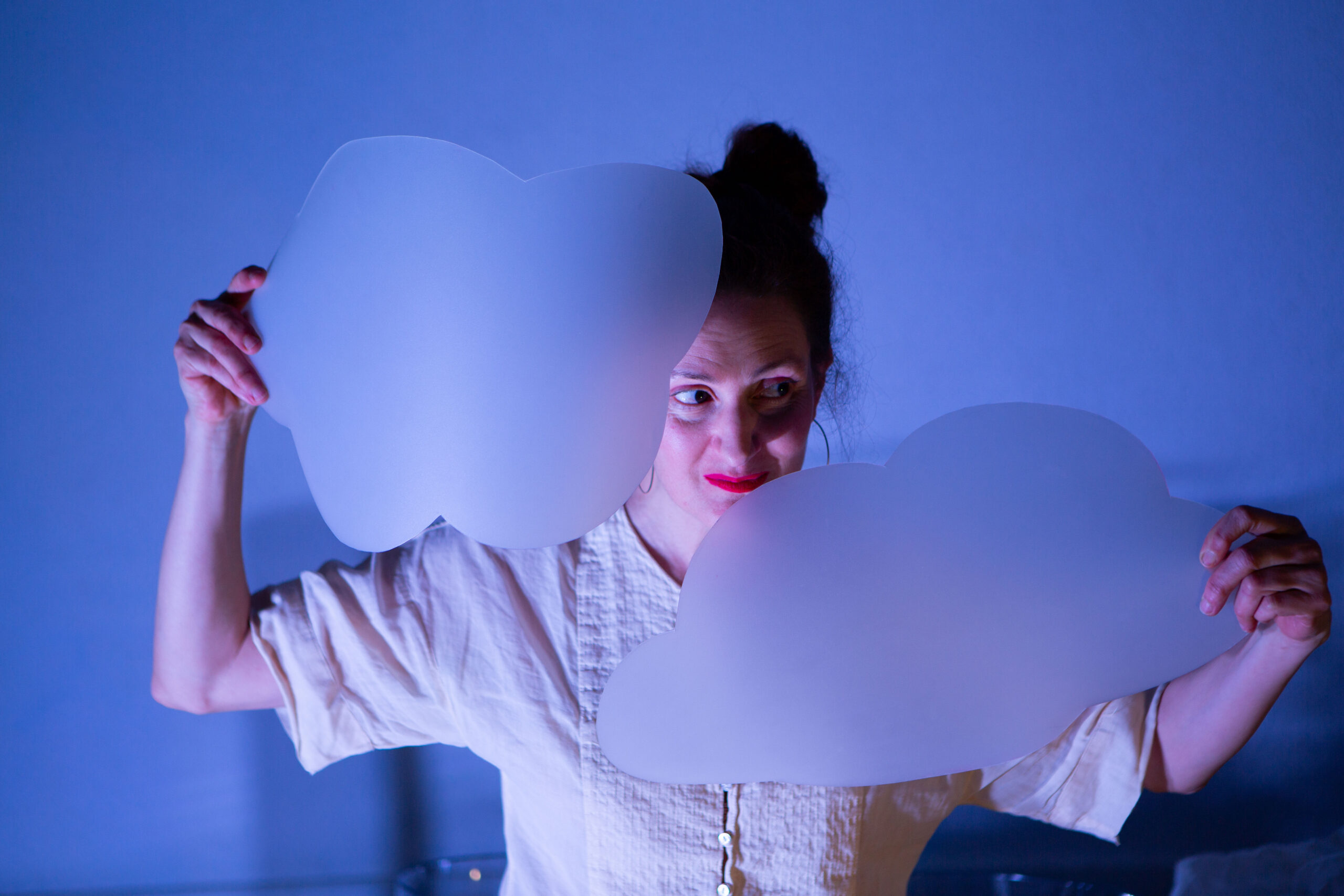 Intérprete sostiene figuras de nubes blancas iluminadas en escena durante el espectáculo “Transparente”.