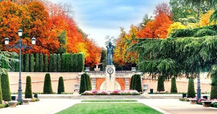 Jardines del Parque del Retiro con monumento central rodeado de árboles otoñales en Madrid.