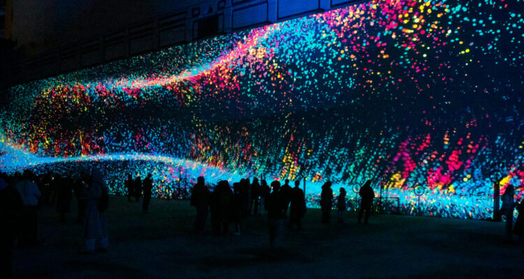 Proyección de ondas de luz de colores en el Frontón Beti Jai durante el festival LuzMadrid con visitantes en el patio.