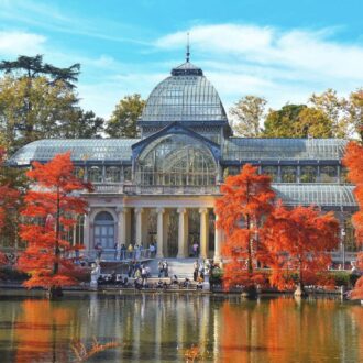 Palacio de Cristal del Parque del Retiro rodeado de árboles otoñales junto al lago en Madrid.