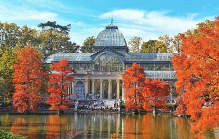 Palacio de Cristal del Parque del Retiro rodeado de árboles otoñales junto al lago en Madrid.