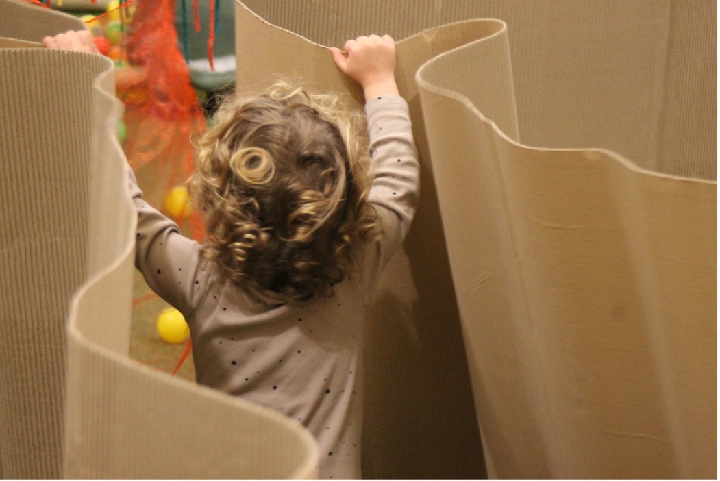 Niño pequeño jugando dentro de una instalación artística de cartón