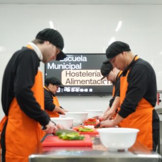 Alumnos de la Escuela Municipal de Hostelería y Alimentación de Madrid preparando verduras en una cocina profesional durante un curso gratuito.