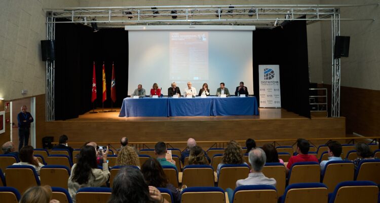 El concejal de Carabanchel, Carlos Izquierdo, durante el I Foro Sueña Carabanchel, acompañado con expertos en una mesa larga, vistos desde el fondo de la sala