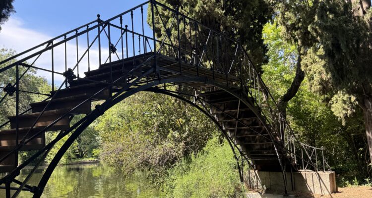 Puente de hierro forjado sobre el estanque del parque de El Capricho de Madrid rodeado de vegetación