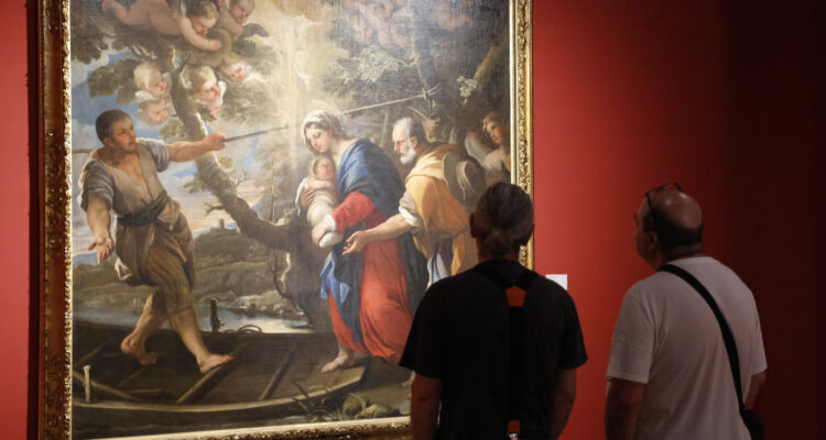 Imagen de dos visitantes de la exposición contemplando una de las piezas