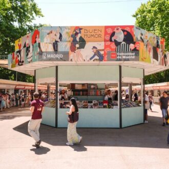 Caseta institucional compartida por el Ayuntamiento de Madrid y la Comunidad de Madrid en la 85ª Feria del Libro, decorada con ilustraciones de la temática Buen Humor, rodeada de visitantes