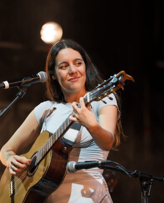 Valeria Castro sonriendo mientras toca la guitarra en el escenario de Conde Duque