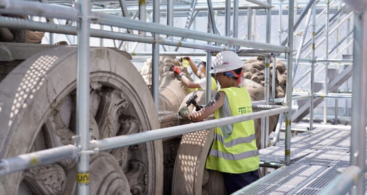 Dos restauradoras trabajando entre los andamios junto a las ruedas del carro y los leones de la Fuente de Cibeles