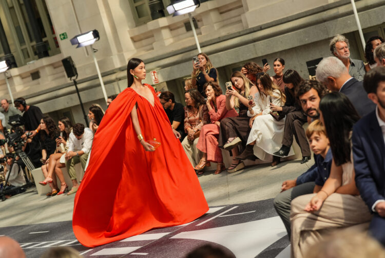 Imagen del desfile de la semana de la moda 2025 con una mujer desfilando con un vestido largo rojo