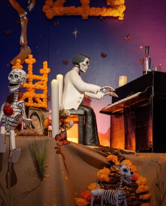 Figura de Agustín Lara representado como una calavera tocando el piano, rodeado de flores de cempasúchil y elementos tradicionales del Día de Muertos