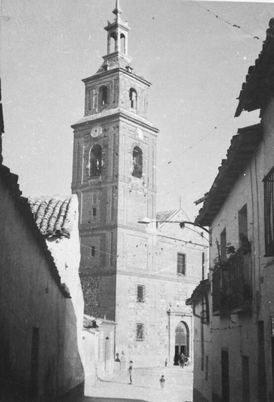 Fotografía antigua de la torre de la iglesia de Santa María la Antigua de Vicálvaro, entre casas tradicionales del pueblo.